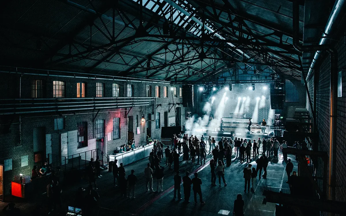 A party in a brick industrial hall, stage light through the haze, guests and a bar