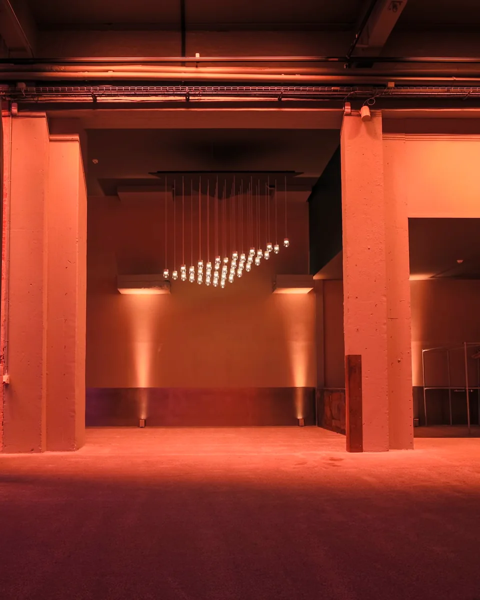 An empty industrial event space in warm light, a hanging light installation between concrete pillars